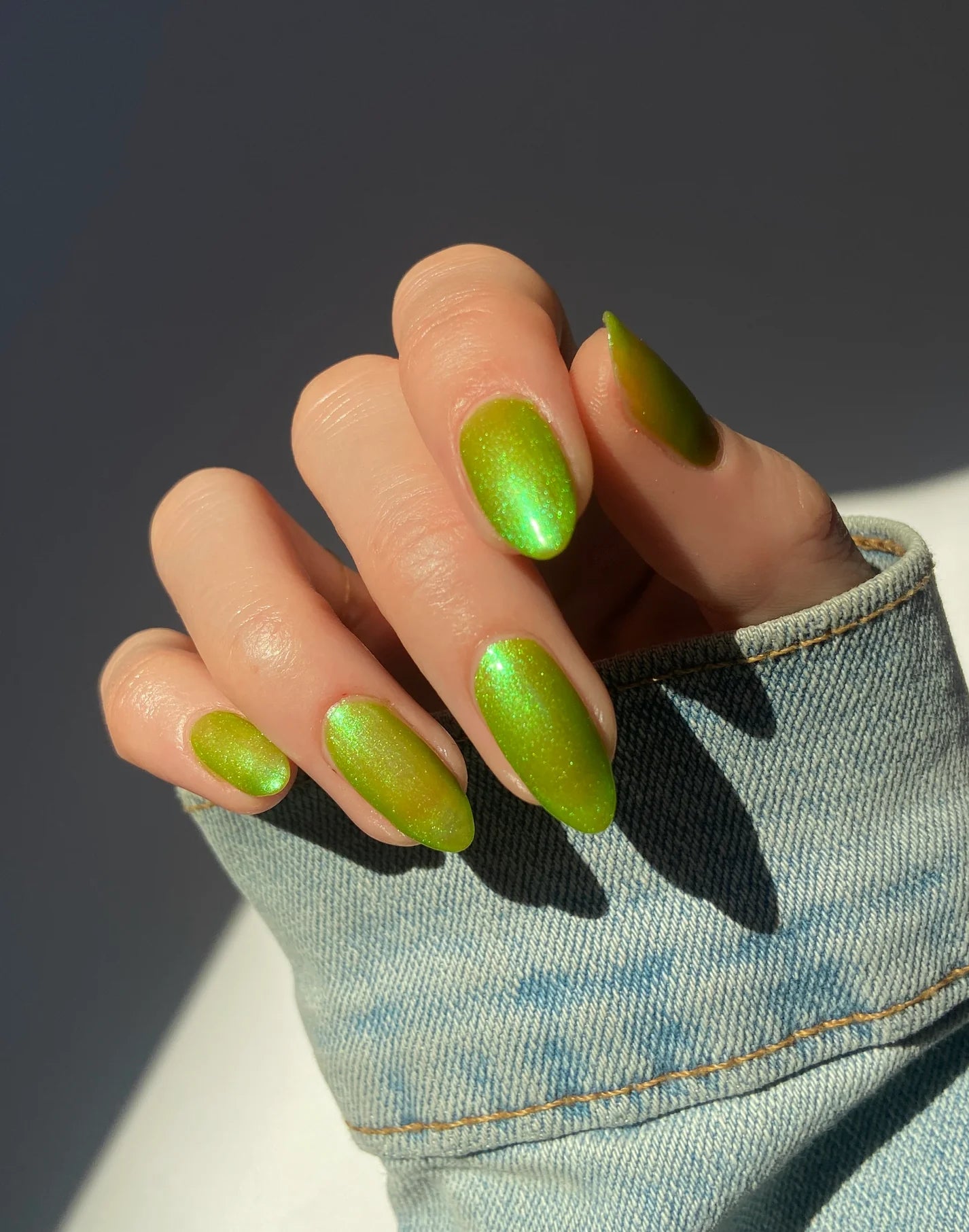 Hand with green nail polish wearing a denim sleeve against a dark background