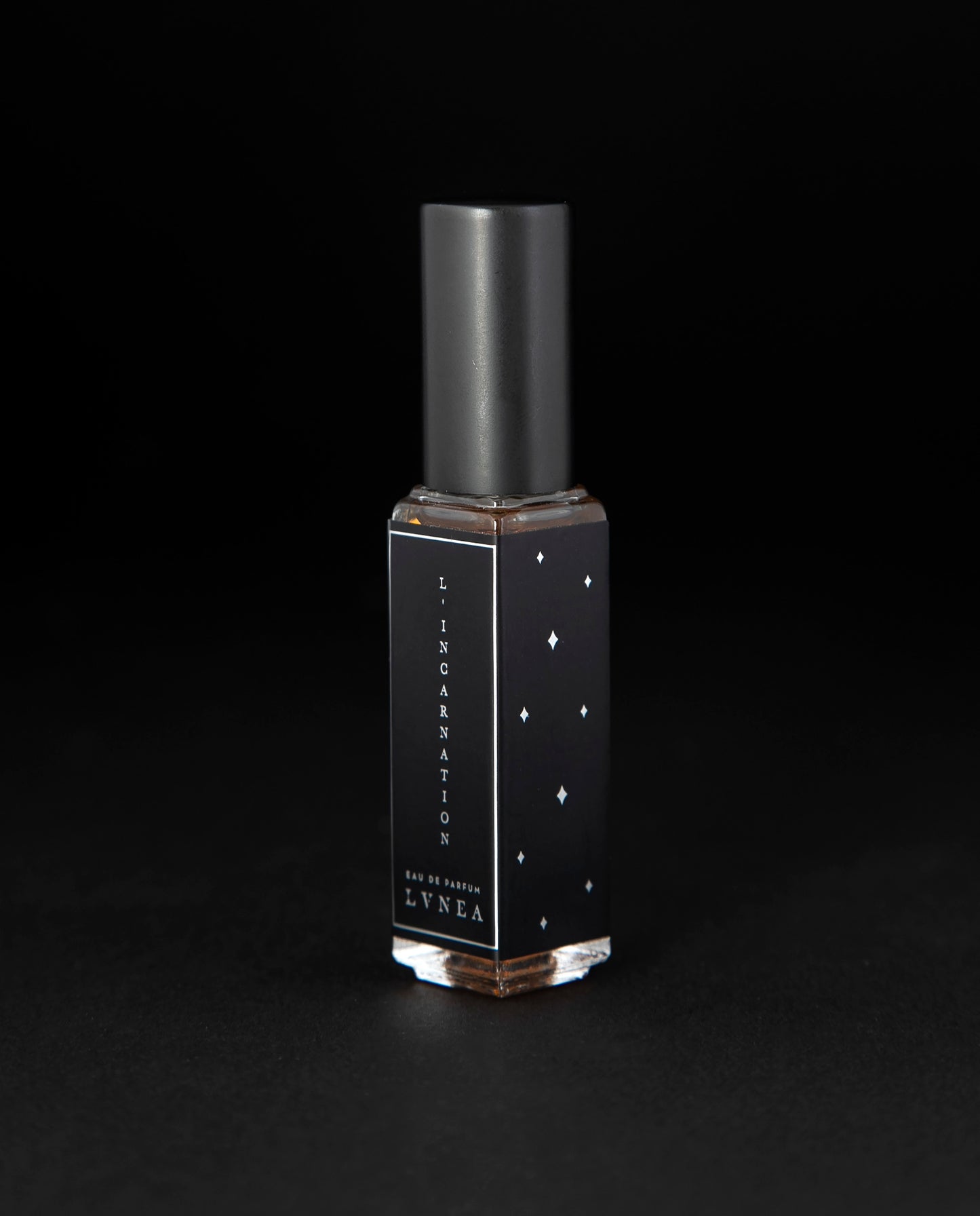 8ml clear bottle of LVNEA'S L'Incarnation natural perfume on black background, bottle is rotated at a 3/4 angle exposing a star pattern on the label.