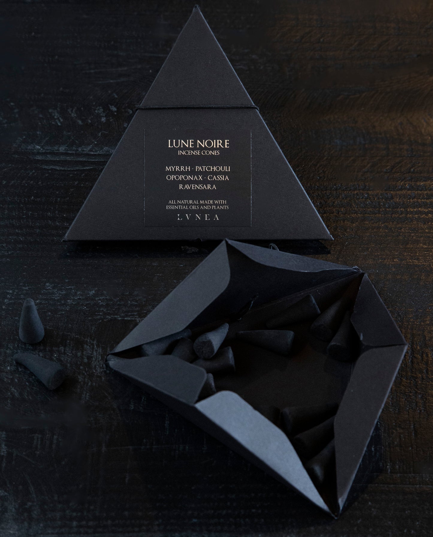 Two black paper pyramid boxes with black elastic closure containing LVNEA’s Lune Noire incense. One of the boxes is open, revealing the charcoal incense cones within.
