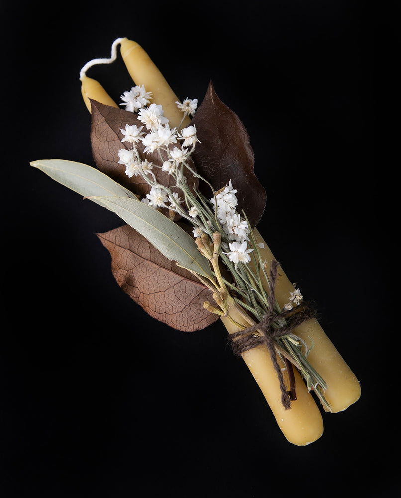 two beeswax tapers bundled with a small bouquet of autumnal botanicals