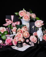 Abundant rose-filled still life featuring each items from LVNEA's "Rose Devotion" Limited Edition Amatory Box surrounded by Venusian white milkglass, fresh pink roses, and greenery.