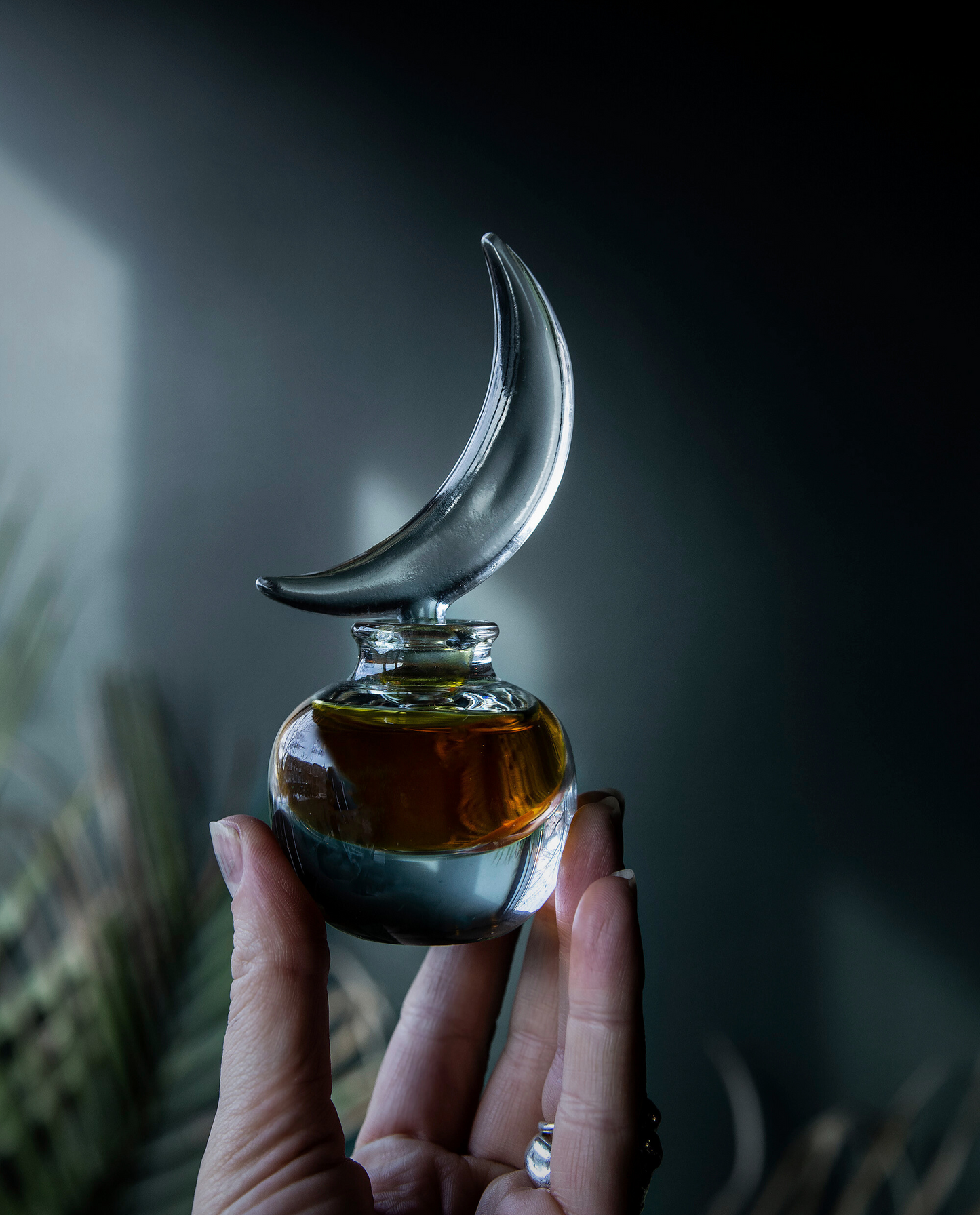 Glass perfume bottle with a crescent moon design held by a hand against a dark background