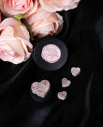 Black tin of LVNEA's "Ardent Hearts" incense seen from overhead on a black piece of satin. The tin is surrounded by loose heart-shaped incense pastilles and pink roses