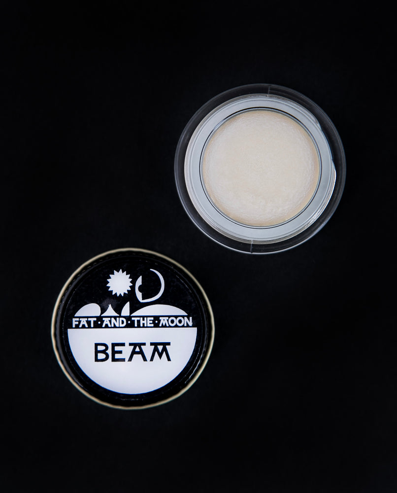 open glass pot of Fat and the Moon's "Beam" highlighter, revealing a shimmery white makeup product
