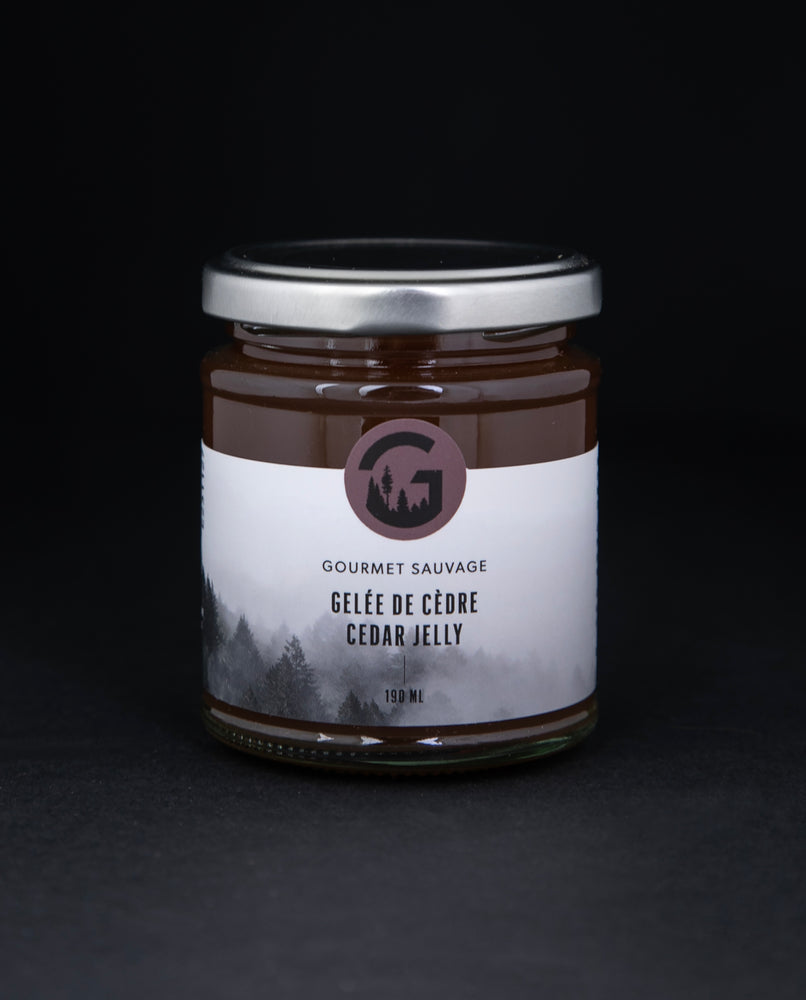 Clear glass jar with metal lid of Gourmet Sauvage's cedar jelly, sitting on black background