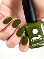 Close up of nails painted with Death Valley Nails' "Crocodilia" nail polish, holding bottle of the product.
