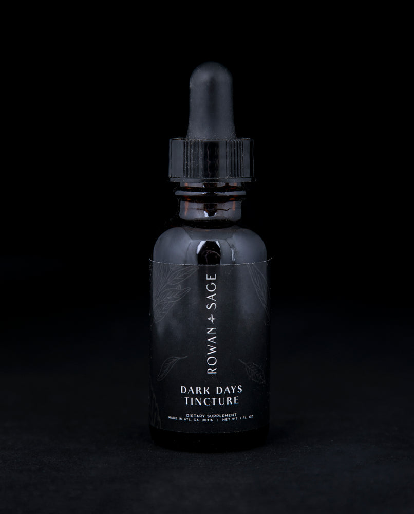 1oz amber glass bottle with dropper top and black label, containing Rown + Sage's "Dark Days" tincture on black background.