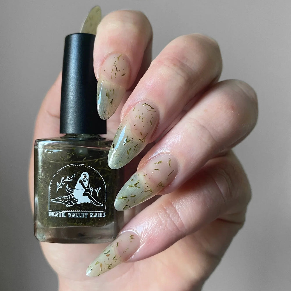 Close up of nails painted with Death Valley Nails' "Dill Weed" nail polish, holding a bottle of the product.