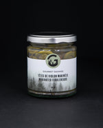 Clear glass jar with metal lid of Gourmet Sauvage's marinated fiddleheads, sitting on black background