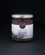 Clear glass jar with metal lid of Gourmet Sauvage's balsam fir jelly, sitting on black background
