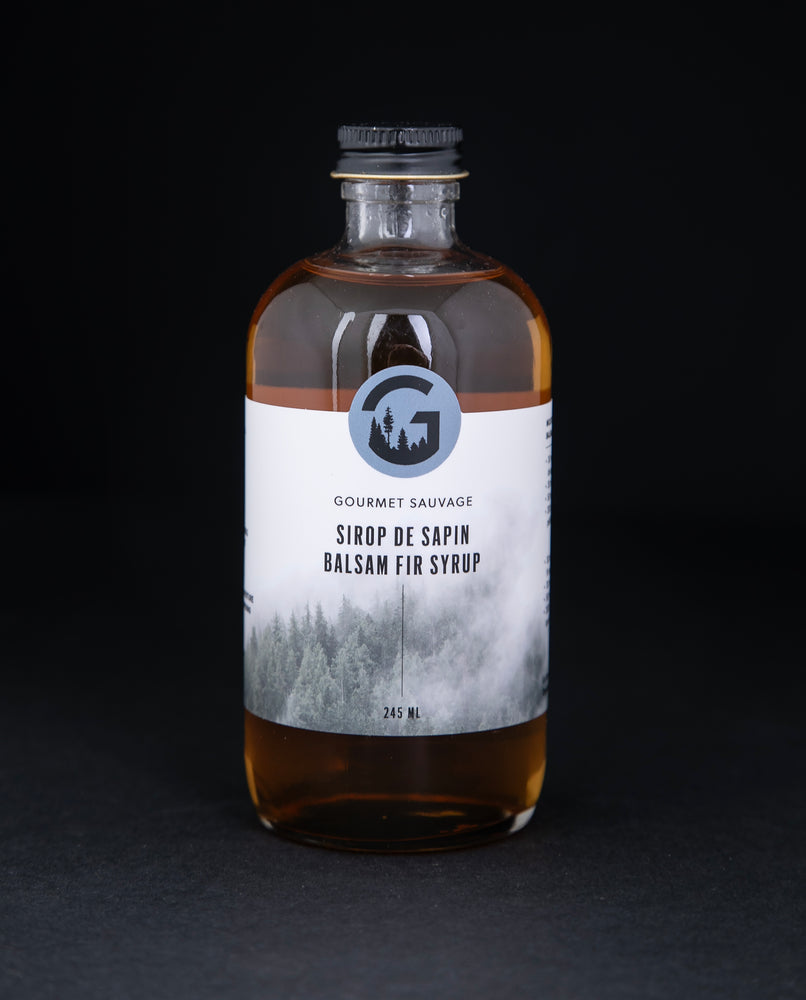 Clear bottle of Gourmet Sauvage's balsam fir syrup, sitting on black background