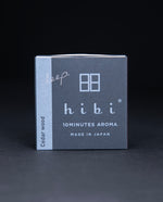 Dark slate grey paper box containing HIBI "cedarwood" incense matches, sitting on black background