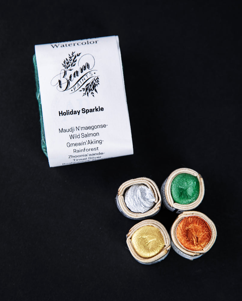 Beam Paints' "Holiday Sparkle" watercolour paint stones sitting on a black background next to their paper and waxed canvas packaging. 