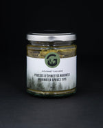 Clear glass jar with metal lid of Gourmet Sauvage's marinated spruce tips, sitting on black background