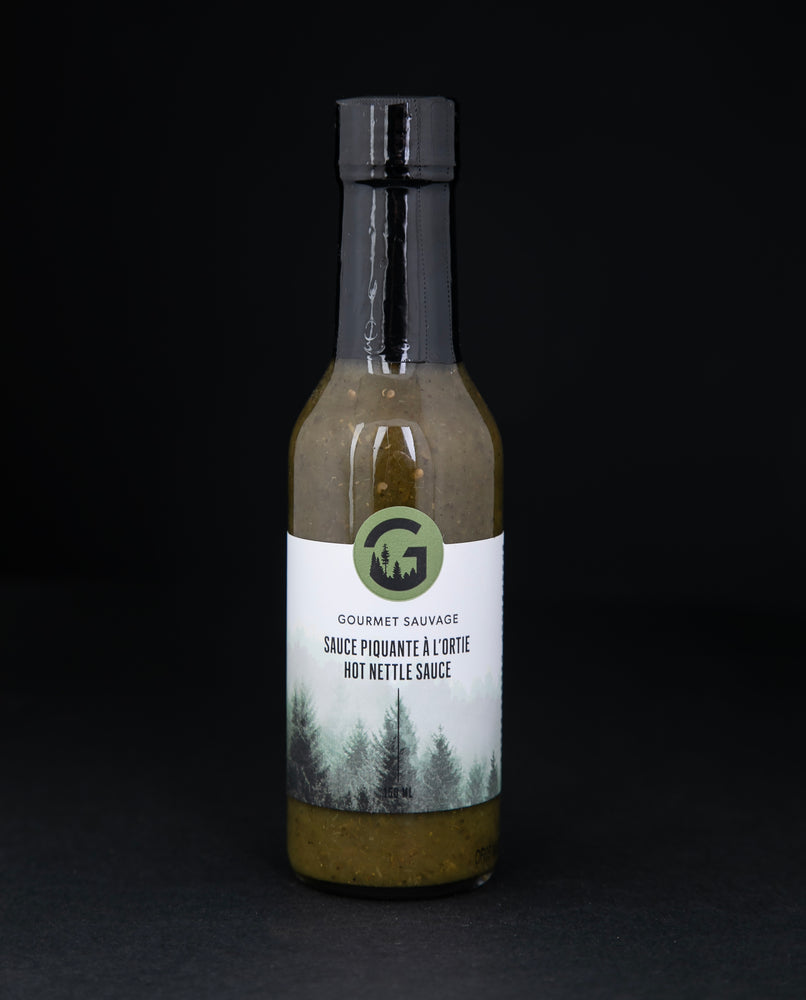 Clear glass bottle of Gourmet Sauvage's nettle hot sauce, sitting on black background