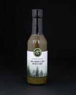 Clear glass bottle of Gourmet Sauvage's nettle hot sauce, sitting on black background