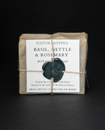 Bar of Naturasophia soap wrapped in brown paper and twine, with a label that reads "Basil, Nettle & Rosemary". There is a deep green wax stamp holding the label in place.