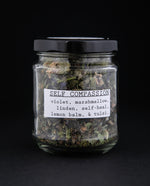 Clear glass jar of Blueberryjams' "Self Compassion" herbal tea blend against black background