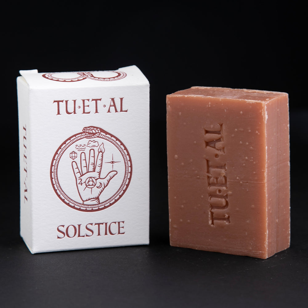 
                      
                        Box and bar of TU-ET-AL's "Solstice" soap sitting against a black background. The bar of soap is a rust colour.
                      
                    