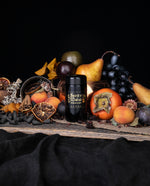 Black glass jar of LVNEA's Spirit of Misrule incense cones. Surrounded by an assortment of orange of yellow fruits, including persimmon, yellow pear, fresh and dried apricot, and dried orange slices.