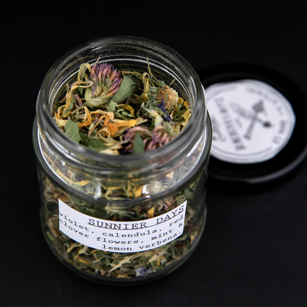 
                      
                        Open jar of "Sunny Days" herbal tea blend, colourful calendula, red clover, and violet flowers are visible
                      
                    