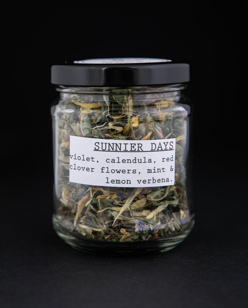 Clear glass jar of Bleuberryjams Sunnier Days herbal tea on black background
