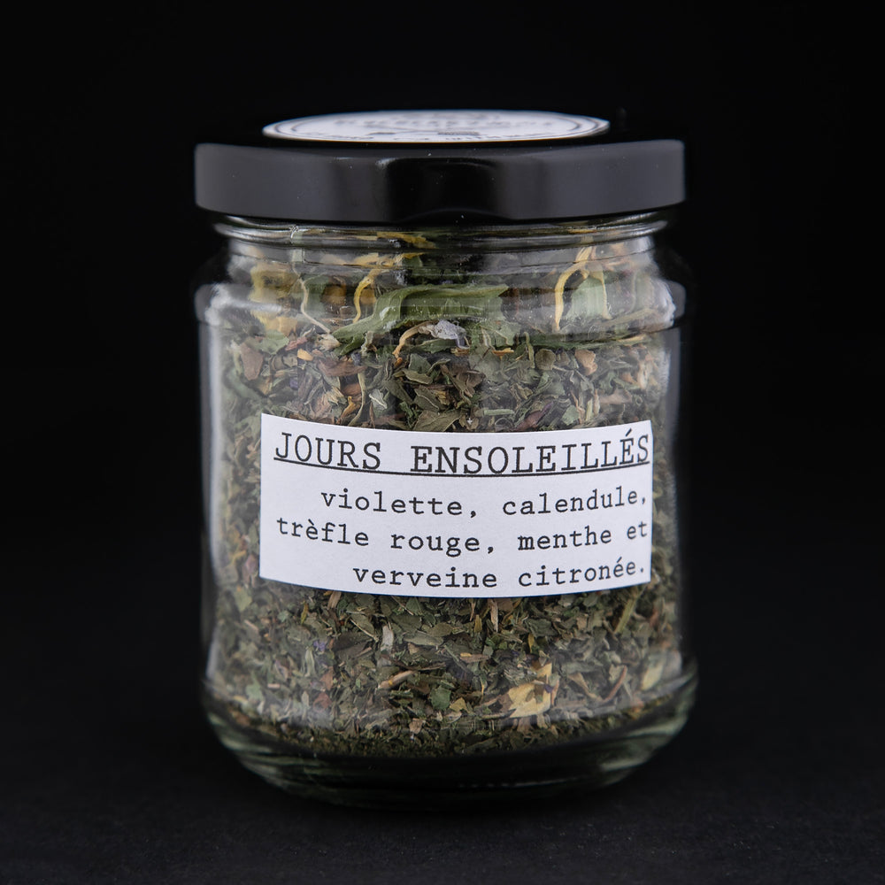 
                      
                        Clear glass jar of Bleuberryjams Sunnier Days herbal tea on black background, french side of the label is showing and reads "Jours Ensoleillés"
                      
                    