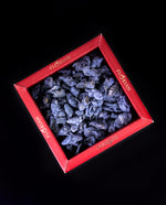 Crystallized edible violet petals presented in a red box with gold foil, shot on a black background