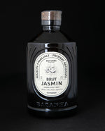 Ornate black glass bottle of Bacanha's Jasmine simple syrup on black background.