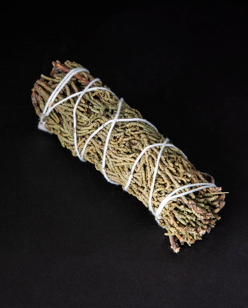 bundle of dried juniper wrapped in white string on black background.