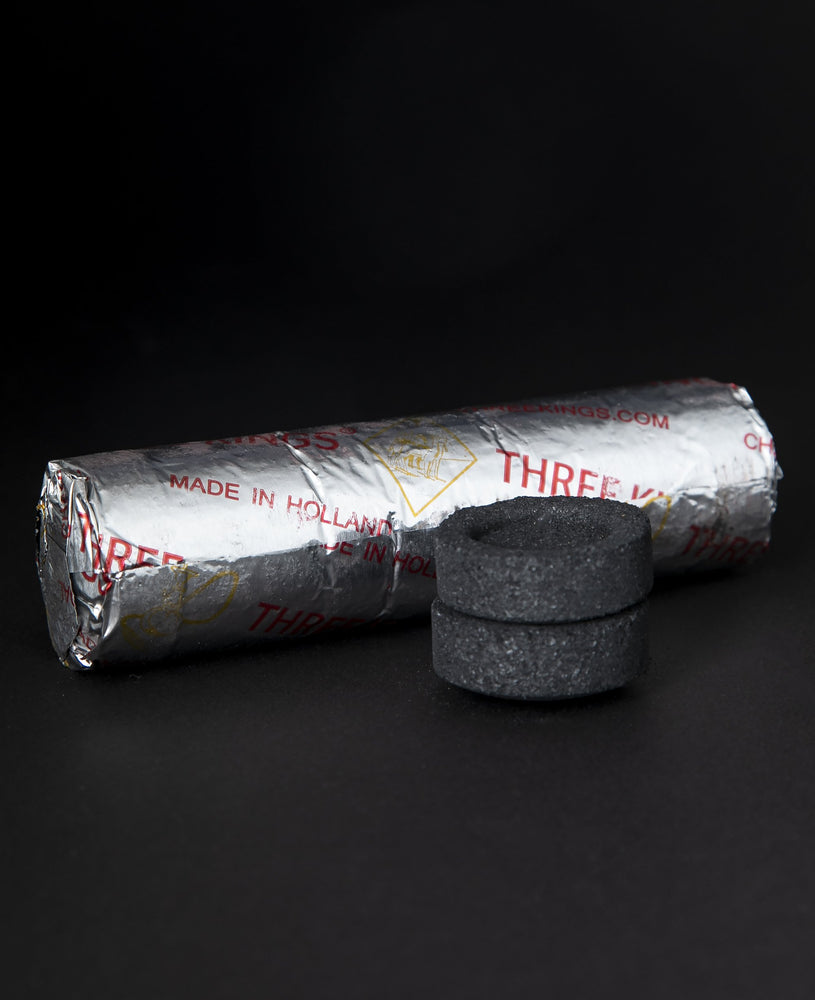two charcoal discs stacked on top on one another, with a silver-foiled package of charcoal lying behind them