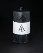 Short black beeswax pillar candle by RITUAALIA on black background. The candle has a rustic textured finish with visible drips.