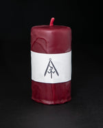 Short scarlet red beeswax pillar candle standing on black background. The candle has a natural handmade finish with a drip texture.