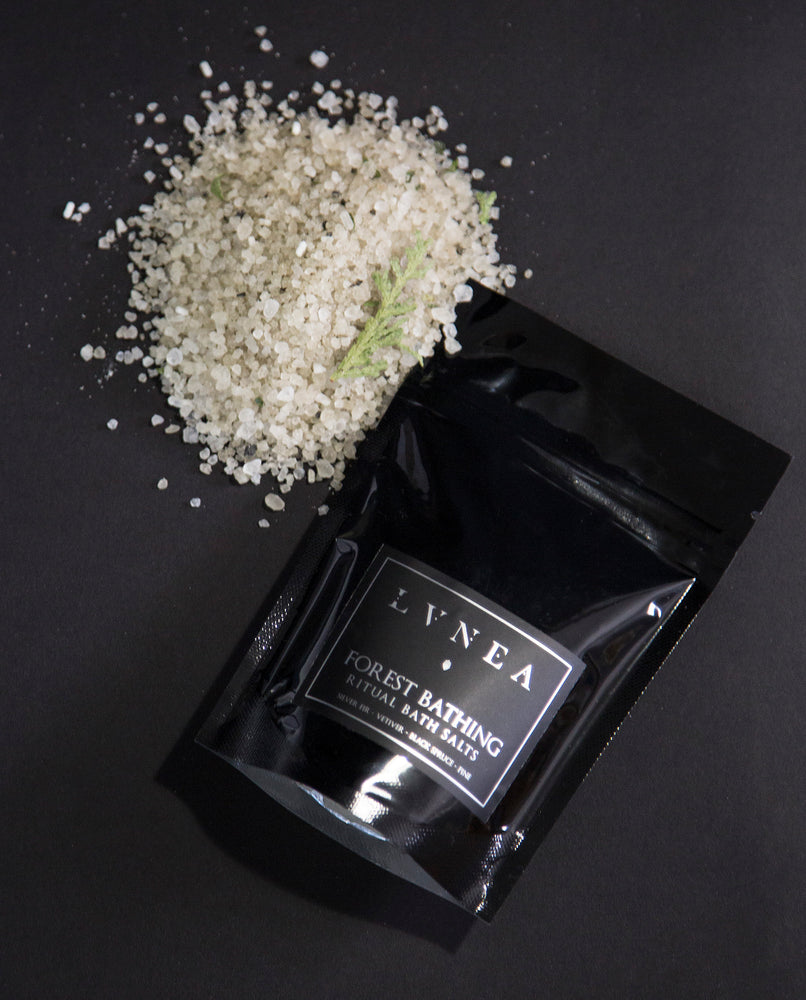4oz black resealable pouch of LVNEA's Forest Bathing bath salts with a mound of green-hued salt next to it
