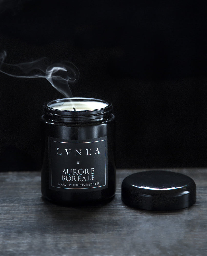 Aurore Boréale candle housed in a resealable 8 ounce black glass jar. The lid is open revealing a wisp of smoke emerging from the just-extinguished cotton wick.