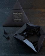 Two black paper pyramid boxes with black elastic closure containing LVNEA’s Solstice d'Hiver incense. One of the boxes is open, revealing the charcoal incense cones within. 