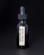 Black glass bottle with dropper top on black background, containing a herbal tincture by blueberryjams. The label is cream coloured and reads "Letting Go / Lâcher Prise".