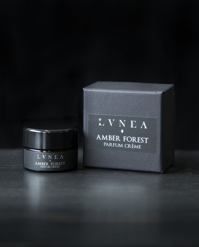 10g black glass jar of LVNEA's 'Amber Forest' vegan solid perfume, sitting next to its black box on a black wooden surface.
