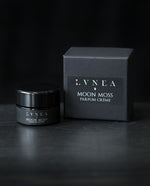 10g black glass jar of LVNEA's 'Moon Moss' vegan solid perfume, sitting next to its black box on a black wooden surface.