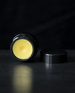 LVNEA's Midnight Tuberose solid perfume on black background. The 10g black glass pot is open and reveals a golden cream perfume.