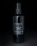A 100% natural hydrosol or aromatherapeutic face and body mist  by LVNEA housed in a 100ml black glass bottle with spray top. The label reads DAMASK ROSE FLORAL WATER in silver in english and french. 