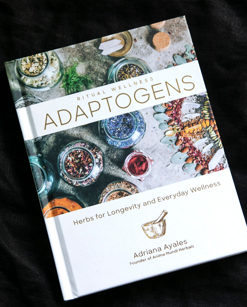 Adriana Ayales' book "Adaptogens" on a black background. The cover is white with a photo of jars of colourful herbs and botanicals on it.