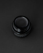 Black-tinted lip balm in a 5g black glass pot on a black background