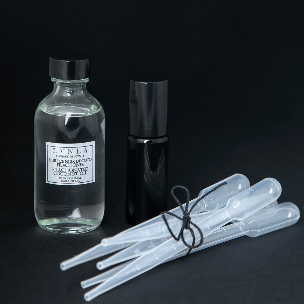 Clear 60ml glass bottle of fractionnated coconut oil, a 10ml black glass roller, and 5 clear plastic pipettes bundled together with a piece of black twine.