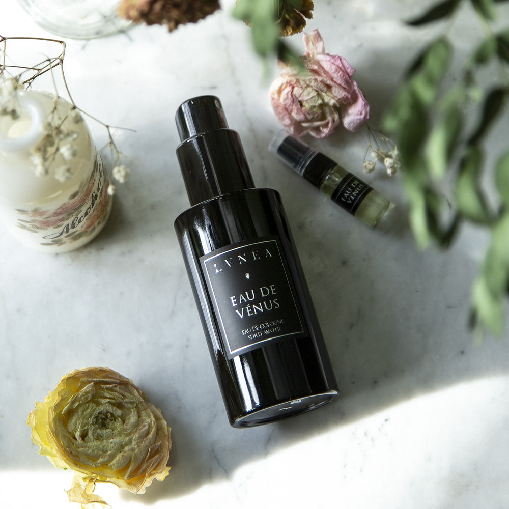 
                      
                        100ml black bottle and sample vial of LVNEA'S Eau de Venus fragrance lying on white marble surrounded by dried florals and botanicals
                      
                    