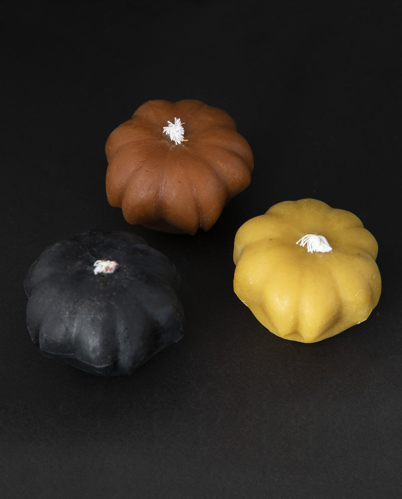 Trio of small beeswax candles shaped like pumpkins. One is black, one is orange, one is golden.