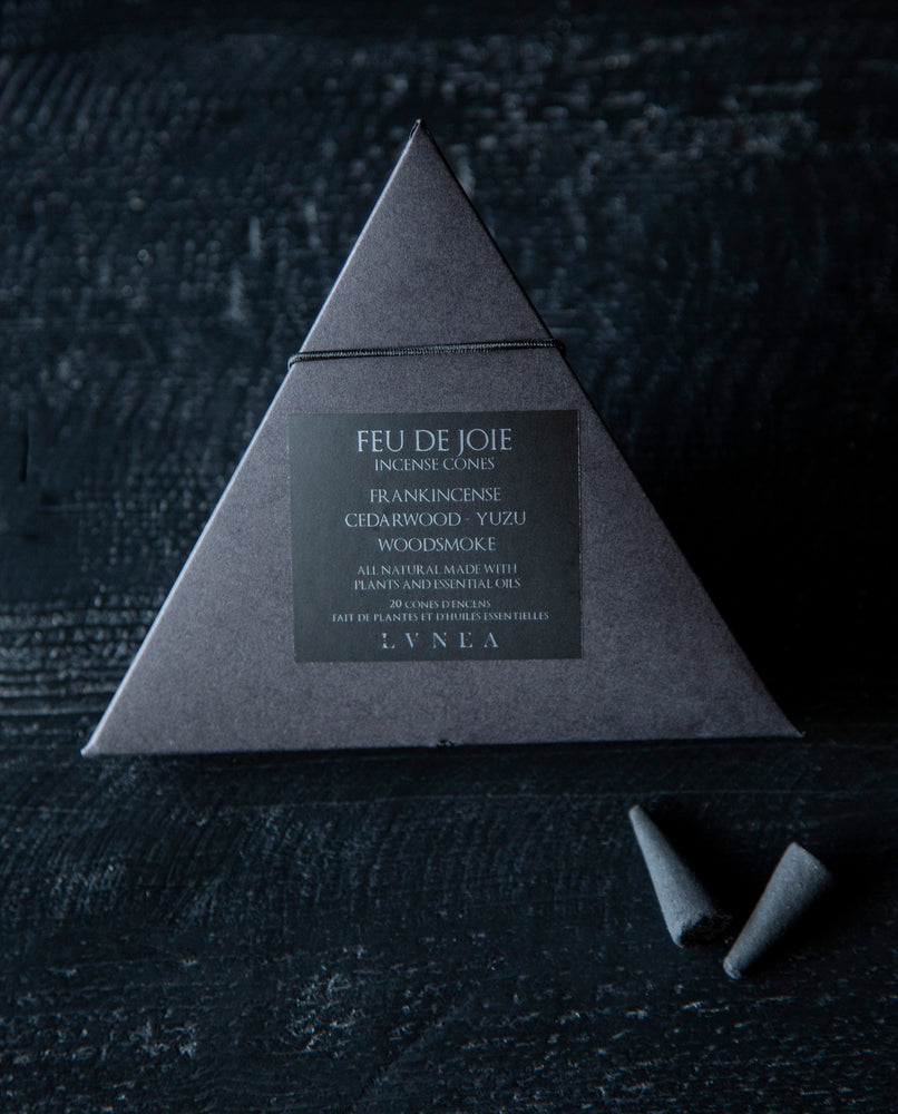 Feu de joie is a naturally perfumed charcoal coal incense with notes of soft woods and smoke, aromatic dark citrus, with a balsamic sweetness. Features LVNEA's essential oil blend of frankincense, cedarwood, yuzu, and woodsmoke. The 20 cones are housed in a recyclable black paper pyramid box with a black elastic closure. The label is black with silver lettering that reads: Feu de Joie incense cones. Frankincense, cedarwood, yuzu, woodsmoke. All natural made with essential oils and plants.