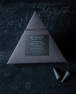 Two black paper pyramid boxes with black elastic closure containing LVNEA’s Feu de Joie incense. One of the boxes is open, revealing the charcoal incense cones within. 