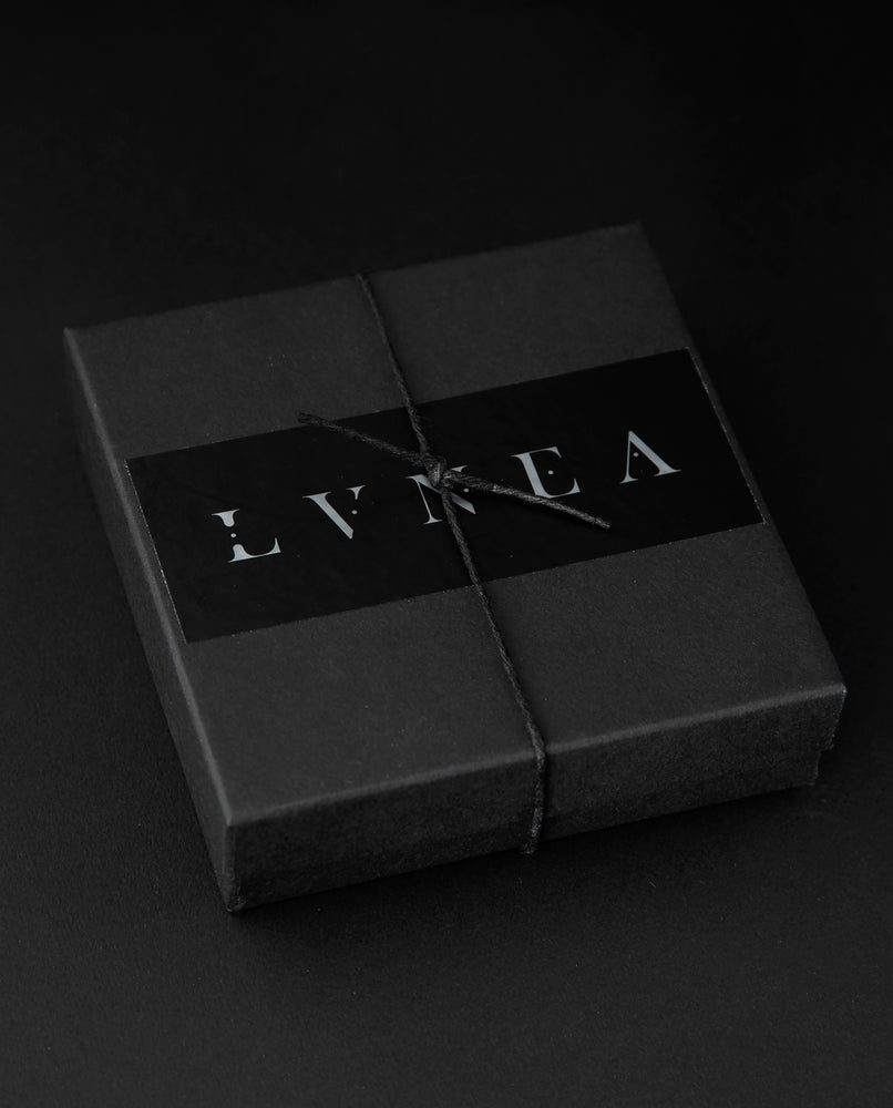 Black box with silver foil LVNEA sticker wrapped in black twine on black background. The box houses the entire oil perfume sample set.
