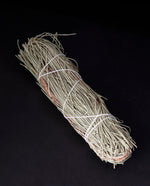 bundle of dried pinon pine wrapped in white string on black background.